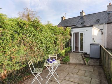 A small patio with two chairs and a table with a tea set next to a building with open doors at Cwrt in Dwyran near Niwbwrch Newborough