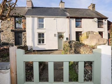 A front yard with a pale green gate and a white two-story house with a wreath on the door and a stone car sculpture at Cwrt in Dwyran near Niwbwrch Newborough