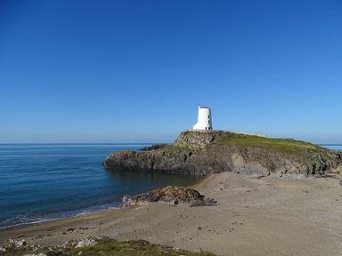 A white tower on a rocky cliff by the sea with a sandy beach in the foreground at Cwrt in Dwyran near Niwbwrch