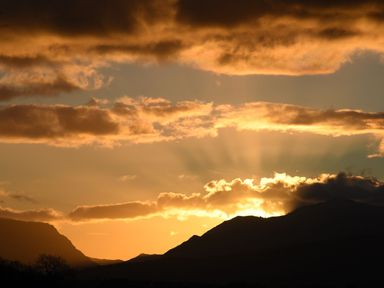 A sunset behind mountain silhouettes with rays of light through clouds at Cwrt in Dwyran near Niwbwrch Newborough