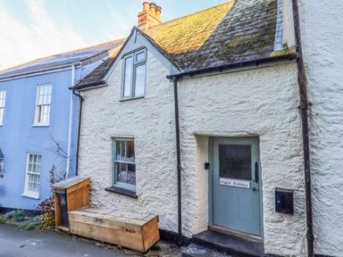 Exterior view of a white textured cottage with a blue door labeled Alpha Cottage in Dittisham near Dartmouth