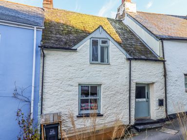A white stone cottage with a mossy roof two windows a blue door and a wooden bench outside at Alpha Cottage in Dittisham near Dartmouth