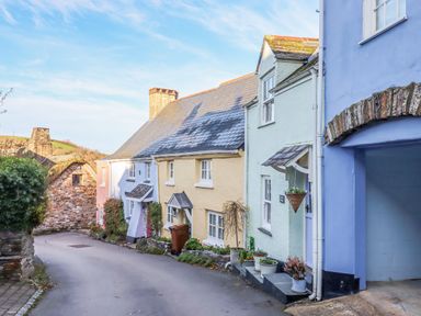 A narrow street with pastel-colored cottages and potted plants at Alpha Cottage in Dittisham near Dartmouth
