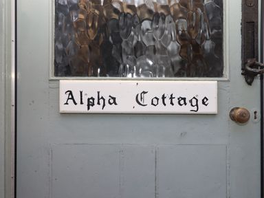 A close up of a blue door with a frosted glass panel and a white sign that says Alpha Cottage