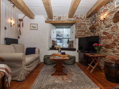 A living room with a beige sofa a wooden coffee table a television and stone walls at Alpha Cottage in Dittisham near Dartmouth