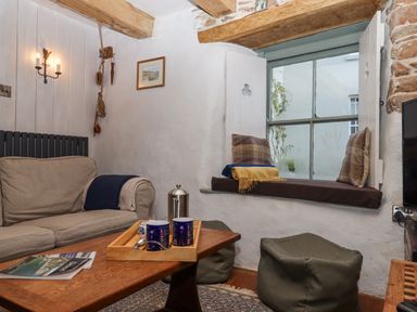 A sitting area with a sofa a wooden table with cups a window seat with cushions and poufs at Alpha Cottage in Dittisham near Dartmouth
