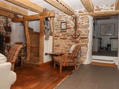 A rustic living area with wooden beams stone walls a staircase chairs and a doorway leading to a kitchen at Alpha Cottage in Dittisham near Dartmouth