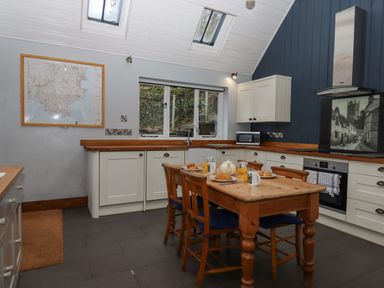 A kitchen with a wooden dining table and chairs a window and map on the wall at Alpha Cottage in Dittisham near Dartmouth