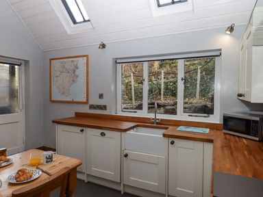 A kitchen with a wooden countertop white cabinets a farmhouse sink a microwave and a table with croissants and orange juice at Alpha Cottage in Dittisham near Dartmouth