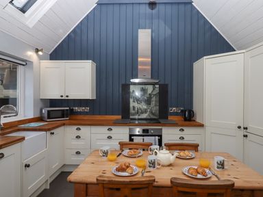 A kitchen with wooden table and chairs set with mugs croissants and glasses of orange juice at Alpha Cottage in Dittisham near Dartmouth