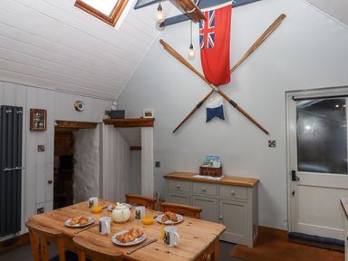 A dining area with a wooden table set for breakfast and crossed oars with flags on the wall at Alpha Cottage in Dittisham near Dartmouth
