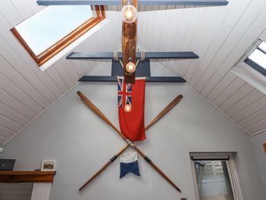 A room ceiling with wooden beams skylights crossed wooden oars and nautical flags on the wall at Alpha Cottage in Dittisham near Dartmouth
