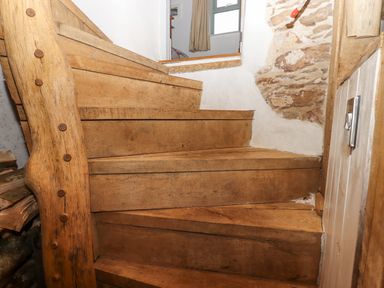 A wooden staircase with thick planks leading to a white wall with exposed stone at Alpha Cottage in Dittisham near Dartmouth