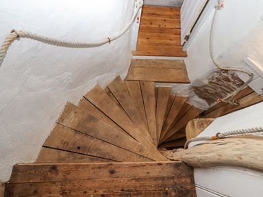 A wooden spiral staircase with rope handrails in a narrow white plaster hallway at Alpha Cottage in Dittisham near Dartmouth