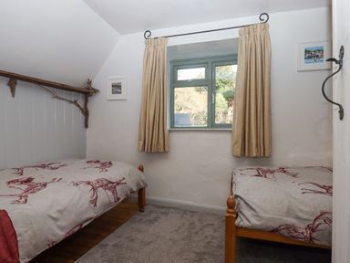 A small bedroom with two single beds and a window with curtains at Alpha Cottage in Dittisham near Dartmouth