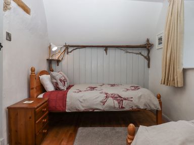 A bedroom with a wooden bed and nightstand a lamp on a small wall shelf and a wood beam decoration at Alpha Cottage in Dittisham near Dartmouth
