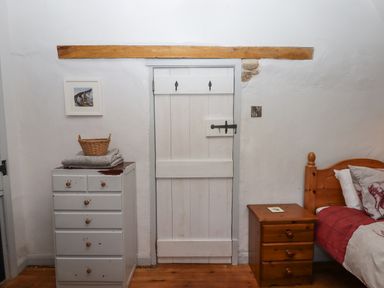 A bedroom corner with a white wooden door between a white chest of drawers and a wooden bedside table next to a bed at Alpha Cottage in Dittisham near Dartmouth