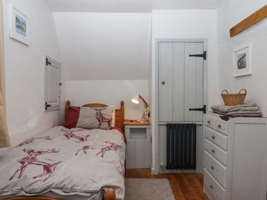 A small bedroom with a single bed a bedside table a lamp a chest of drawers with folded towels and a basket at Alpha Cottage in Dittisham near Dartmouth