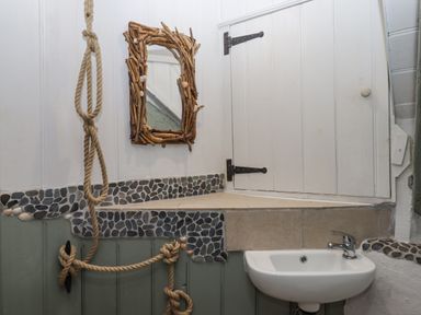 A small bathroom with a white sink a mirror with a wooden frame rope decoration and pebble tile detail at Alpha Cottage in Dittisham near Dartmouth