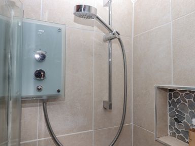 A shower with a chrome showerhead and control panel mounted on tiled walls at Alpha Cottage in Dittisham near Dartmouth