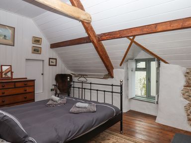 A bedroom with a black metal bed frame wooden beams a wooden chest of drawers and a small window at Alpha Cottage in Dittisham near Dartmouth
