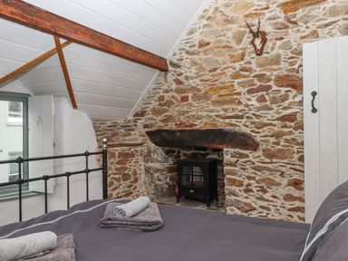 A bedroom with a stone wall fireplace bed with towels and a window at Alpha Cottage in Dittisham near Dartmouth