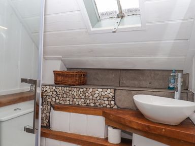 A small bathroom with a white bowl sink on a wooden countertop and a wicker basket on a built-in shelf near a window at Alpha Cottage in Dittisham near Dartmouth