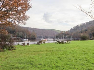 A riverside area with benches and picnic tables near moored sailboats at Alpha Cottage in Dittisham near Dartmouth