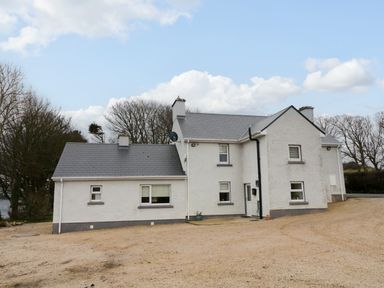 A white two story house with multiple windows and a gray roof on a gravel area surrounded by trees at Dock at Dominic's Ballyheerin near Downings
