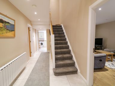 A hallway with carpeted stairs and a gray runner rug next to a living room with a television and wooden coffee table at Dock at Dominic's in Ballyheerin near Downings