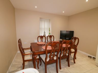 A dining room with a wooden table and six chairs a small window a television and two metal bowls on the floor at Dock at Dominic's Ballyheerin near Downings