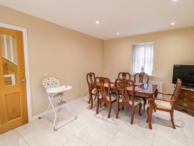 A dining room with a wooden dining table and chairs a high chair a window and a television with a stand at Dock at Dominic's Ballyheerin near Downings