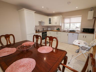A kitchen with white cabinets and wooden countertops a wooden dining table with pink placemats and a white high chair at Dock at Dominic's in Ballyheerin near Downings