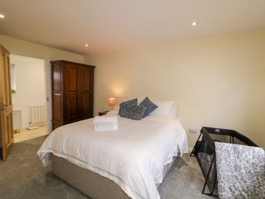A bedroom with a bed with white bedding and pillows a wooden wardrobe a bedside table with a lamp and a baby crib at Dock at Dominic's in Ballyheerin near Downings