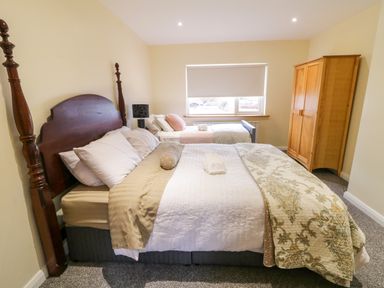 A bedroom with two beds a wooden wardrobe a window with a blind and a bedside table with a lamp at Dock at Dominic's in Ballyheerin near Downings
