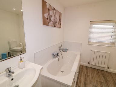 A bathroom with a bathtub a sink a toilet reflected in a mirror a window with blinds and a wall-mounted radiator at Dock at Dominic's Ballyheerin near Downings