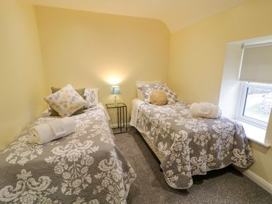 A bedroom with two single beds with patterned bedspreads a small lamp on a side table and a window with a roller blind at Dock at Dominic's Ballyheerin near Downings