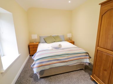A bedroom with a double bed with two pillows and two bedside tables with lamps and a wooden wardrobe by the side at Dock at Dominic's Ballyheerin near Downings