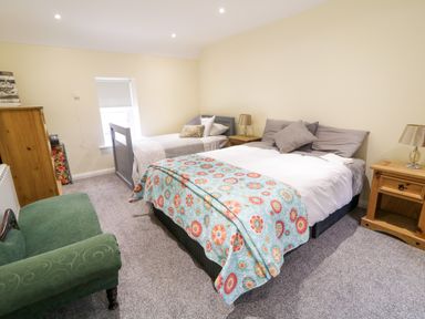 A bedroom with a double bed and single bed with pillows two wooden nightstands with lamps a green armchair and a wooden chest of drawers at Dock at Dominic's in Ballyheerin near Downings