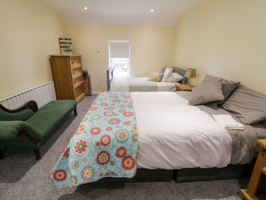 A bedroom with two beds a green chaise lounge a wooden chest of drawers and a nightstand with a lamp at Dock at Dominic's Ballyheerin near Downings