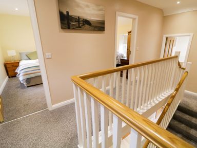 A hallway with carpeted stairs and wooden handrails with doors leading to bedrooms at Dock at Dominic's Ballyheerin near Downings