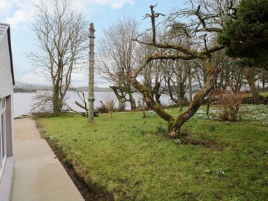 A garden with grass trees and a pathway beside a house near a body of water at Dock at Dominic's Ballyheerin near Downings