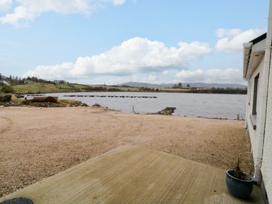 An outdoor area with a concrete and gravel surface next to a body of water with hills in the background at Dock at Dominic's in Ballyheerin near Downings