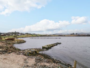 A shoreline with rocks and a body of water with a floating dock and houses in the distance at Dock at Dominic's Ballyheerin near Downings