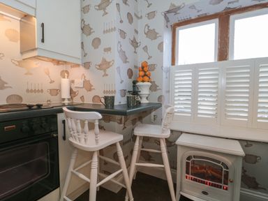 A small kitchen corner with two white high chairs a countertop with cups and a fruit decoration a window with white shutters and an electric stove at Tree Tops in Broadway