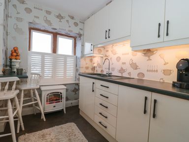 A kitchen with white cabinets a black countertop a sink a coffee machine and a small electric fireplace under a window at Tree Tops in Broadway