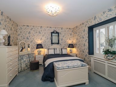 A bedroom with a bed a dresser a vanity table two bedside tables with lamps and a window with shutters at Tree Tops in Broadway