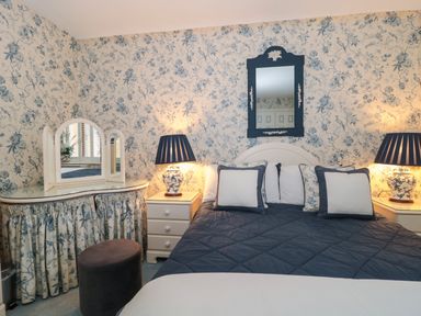 A bedroom with a bed covered with a quilted blanket and pillows between two bedside tables with lamps and a vanity with a mirror at Tree Tops in Broadway