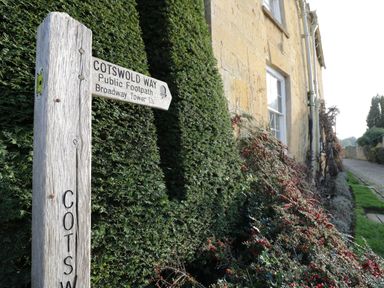 A wooden signpost indicating Cotswold Way public footpath near a stone building with window and greenery at Tree Tops in Broadway
