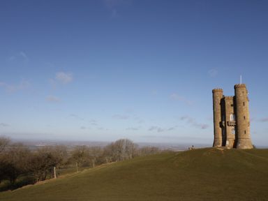 A stone tower on a grassy hill with trees and a clear sky at Tree Tops in Broadway